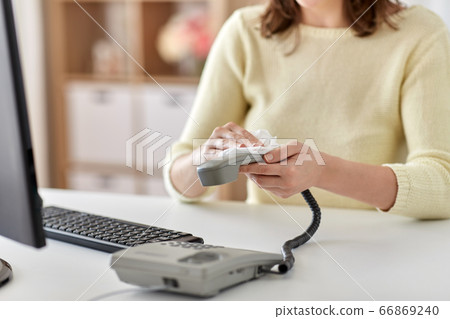 close up of woman cleaning desk phone with tissue 66869240