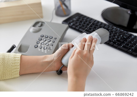 close up of woman cleaning desk phone with tissue 66869242
