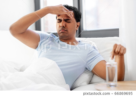sick man in bed with medicine and glass of water sick man in bed with medicine and glass of water 66869695
