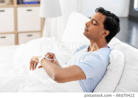 happy indian man with smart watch in bed at home 66870422