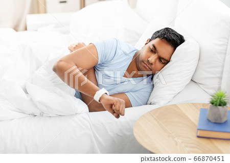 indian man looking at smart watch in bed at home 66870451
