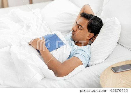 indian man with book sleeping in bed at home 66870453