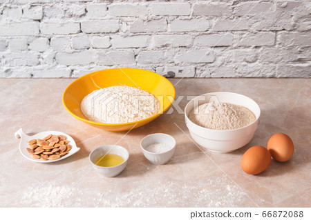 baking ingredients, flour, salt, eggs and oil in white and yellow bowls on marble countertop in bright homey kitchen 66872088