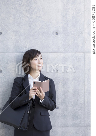 Business woman leaning against the wall with a smartphone 66873283