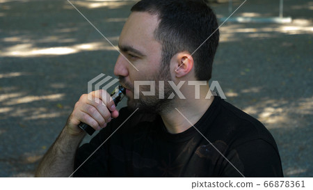 Young man vaping an electronic cigarette for the first time. getting annoyed by the smoke. Young man vaping an electronic cigarette for the first time. getting annoyed by the smoke. 66878361