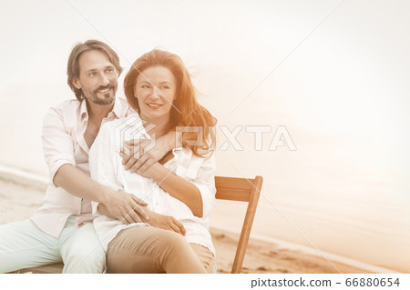 Happy mature couple hugs sitting in beach cafe at sea side. Portrait of hugging pretty two people in love with copy space at right side. Tinted image 66880654