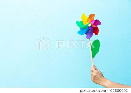 People hold colorful toy plastic turbine windmill on blue background 66880692