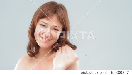 Mature brown-haired female applies skin care cream by touching face with hand, close up. Woman applying anti-age cream on her skin isolated on white background. Spa and wellness concept 66880837
