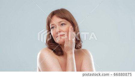 Pretty mature female applies skin care product by touching face with hand. Woman applying anti-age cream on her skin isolated on white background. Spa and wellness concept 66880875