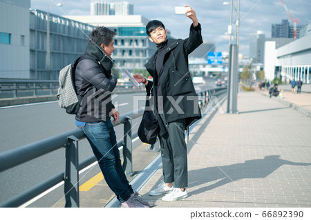 Two young asian men taking selfie while travel with friend in the city Two young asian men taking selfie while travel with friend in the city 66892390