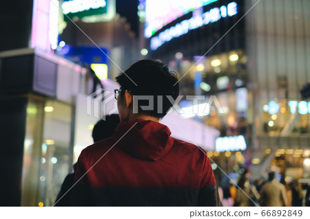 Young man walking in front of department store in big city with bokeh light background at night Young man walking in front of department store in big city with bokeh light background at night 66892849