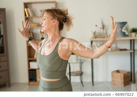 Optimistic middle aged woman in grey elastic tracksuit doing physical exercises Optimistic middle aged woman in grey elastic tracksuit doing physical exercises 66907822