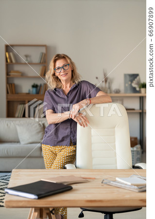 Mature successful businesswoman standing by workplace while staying home 66907899