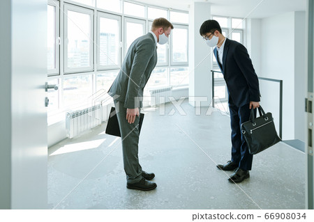 Elegant intercultural businessmen with briefcases greeting each other by bow Elegant intercultural businessmen with briefcases greeting each other by bow 66908034