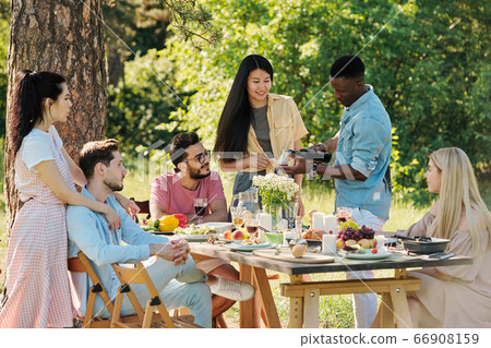 African guy in denim shirt and white jeans pouring red wine into wineglass 66908159