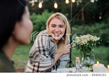 Happy young blond female with toothy smile looking at her friend by served table Happy young blond female with toothy smile looking at her friend by served table 66908181