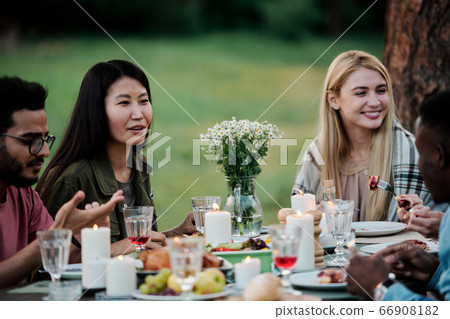Young intercultural females talking to their boyfriends by served table outdoors Young intercultural females talking to their boyfriends by served table outdoors 66908182