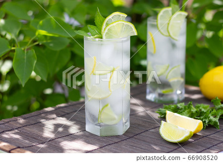 Cold refreshing lemonade or mojito coctail in a glass on gray bamboo and green leaves background. 66908520