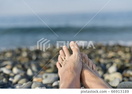 Two bare feet, slightly folded into a hug, against the sea is out of focus. 66913189