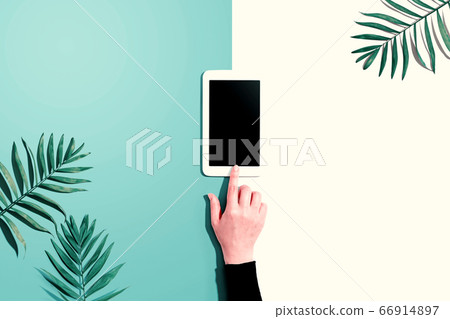 Person using a tablet computer with tropical leaves 66914897