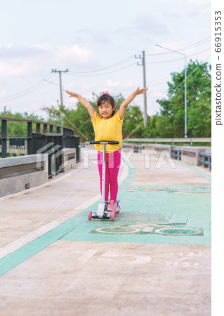 Little child girl to ride scooter in outdoor sports ground on sunny summer day 66915353