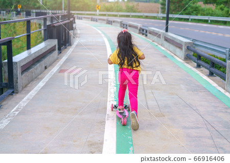 Little child girl to ride scooter in outdoor sports ground on sunny summer day Little child girl to ride scooter in outdoor sports ground on sunny summer day 66916406