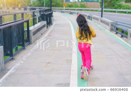Little child girl to ride scooter in outdoor sports ground on sunny summer day Little child girl to ride scooter in outdoor sports ground on sunny summer day 66916408