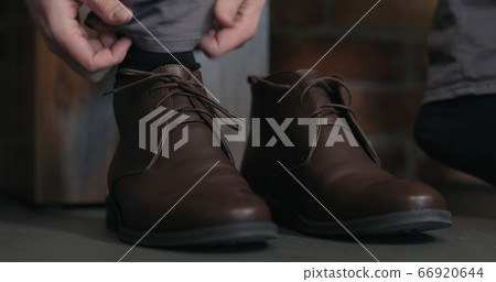 young man lace up his brown leather chukka boots indoor 66920644
