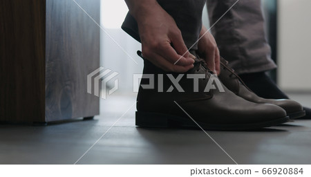 Young man put on his brown leather chukka boots indoor Young man put on his brown leather chukka boots indoor 66920884