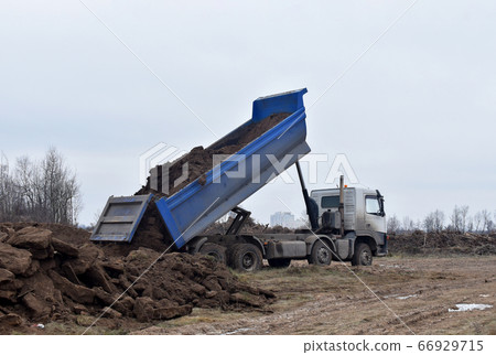 Dump truck dumps its load of sand and ground on construction site for road construction Dump truck dumps its load of sand and ground on construction site for road construction 66929715