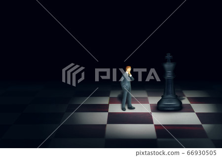 Miniature figure people as businessman standing face to face with King chess piece on chessboard. 66930505