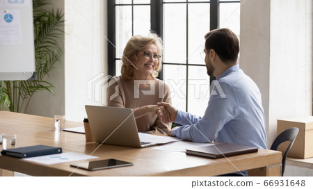 Businessman greeting, shaking mature businesswoman partner hand at meeting Businessman greeting, shaking mature businesswoman partner hand at meeting 66931648