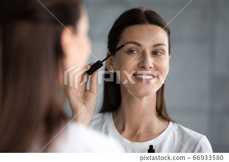 Smiling young woman paint eyelashes with black mascara 66933580