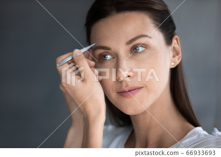 Young woman look in mirror pinch eyebrows with tweezers 66933693
