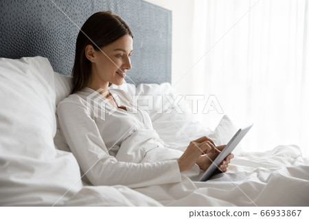 Smiling female relax in bed using tablet Smiling female relax in bed using tablet 66933867