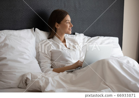 Smiling woman relax in bed working on laptop Smiling woman relax in bed working on laptop 66933871