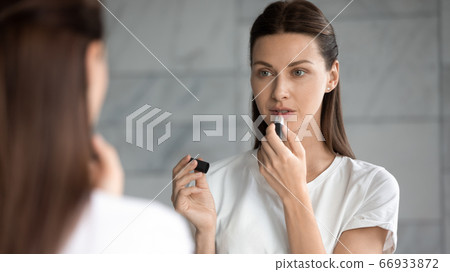 Millennial woman look in mirror paint lips Millennial woman look in mirror paint lips 66933872