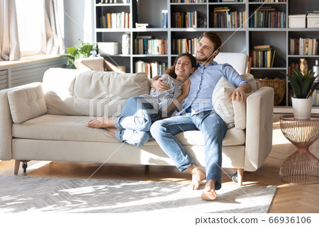 Smiling dreamy young couple relaxing on cozy couch together Smiling dreamy young couple relaxing on cozy couch together 66936106