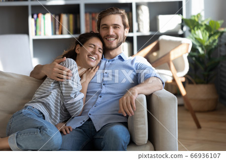 Happy young couple hugging, laughing at joke, sitting on couch 66936107