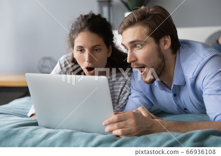 Shocked young couple looking at laptop screen, lying on bed Shocked young couple looking at laptop screen, lying on bed 66936108
