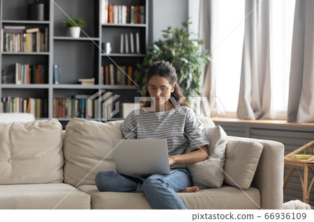 Focused beautiful woman wearing glasses using laptop in living room 66936109