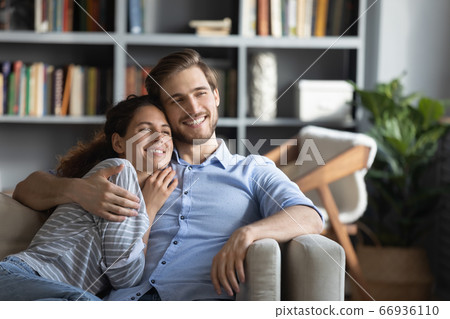 Smiling dreamy young couple hugging, relaxing on couch at home Smiling dreamy young couple hugging, relaxing on couch at home 66936110