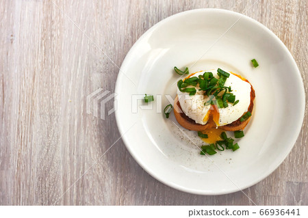 Poached egg, liquid yolk with, green onion on toast bread, white plate on white wooden background 66936441
