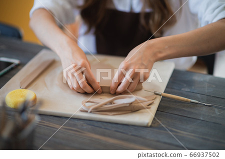 Woman's fingers adding and adjusting a clay part on a future ceramic product. 66937502