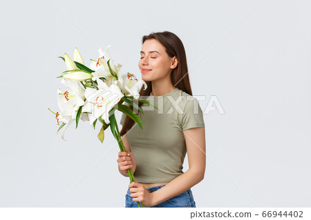 Carefree stylish good-looking woman ordered flowers for home, close eyes smiling and sniffing beautiful bouquet of white lilies, standing satisfied over white background 66944402