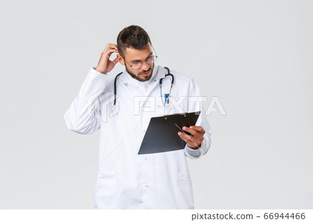 Healthcare workers, medical insurance, clinic lab and covid-19 concept. Thoughtful young doctor in scrubs, glasses, studying patient file, scratch head and look clipboard, reading papers Healthcare workers, medical insurance, clinic lab and covid-19 concept. Thoughtful young doctor in scrubs, glasses, studying patient file, scratch head and look clipboard, reading papers 66944466