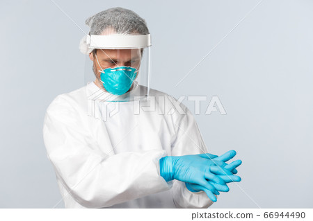 Covid-19, virus, healthcare workers and vaccination concept. Doctor in personal protective equipment put on rubber gloves before entering patient ward with people sick on coronavirus disease 66944490