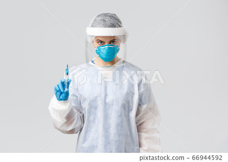 Covid-19, medical research, diagnosis, healthcare workers and quarantine concept. Serious doctor or nurse in personal protective equipment, face shield holding syringe with coronavirus vaccine 66944592