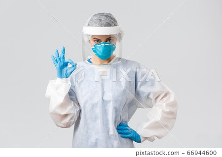 Covid-19, preventing virus, health, healthcare workers and quarantine concept. Serious doctor, professional nurse in PPE, protective suit, respirator and gloves, make okay sign, guarantee Covid-19, preventing virus, health, healthcare workers and quarantine concept. Serious doctor, professional nurse in PPE, protective suit, respirator and gloves, make okay sign, guarantee 66944600