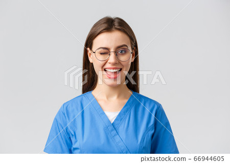 Healthcare workers, medicine, insurance and covid-19 pandemic concept. Cheeky pretty female nurse, intern or doctor in clinic, wear scrubs and glasses, wink at camera with enthusiastic smile 66944605